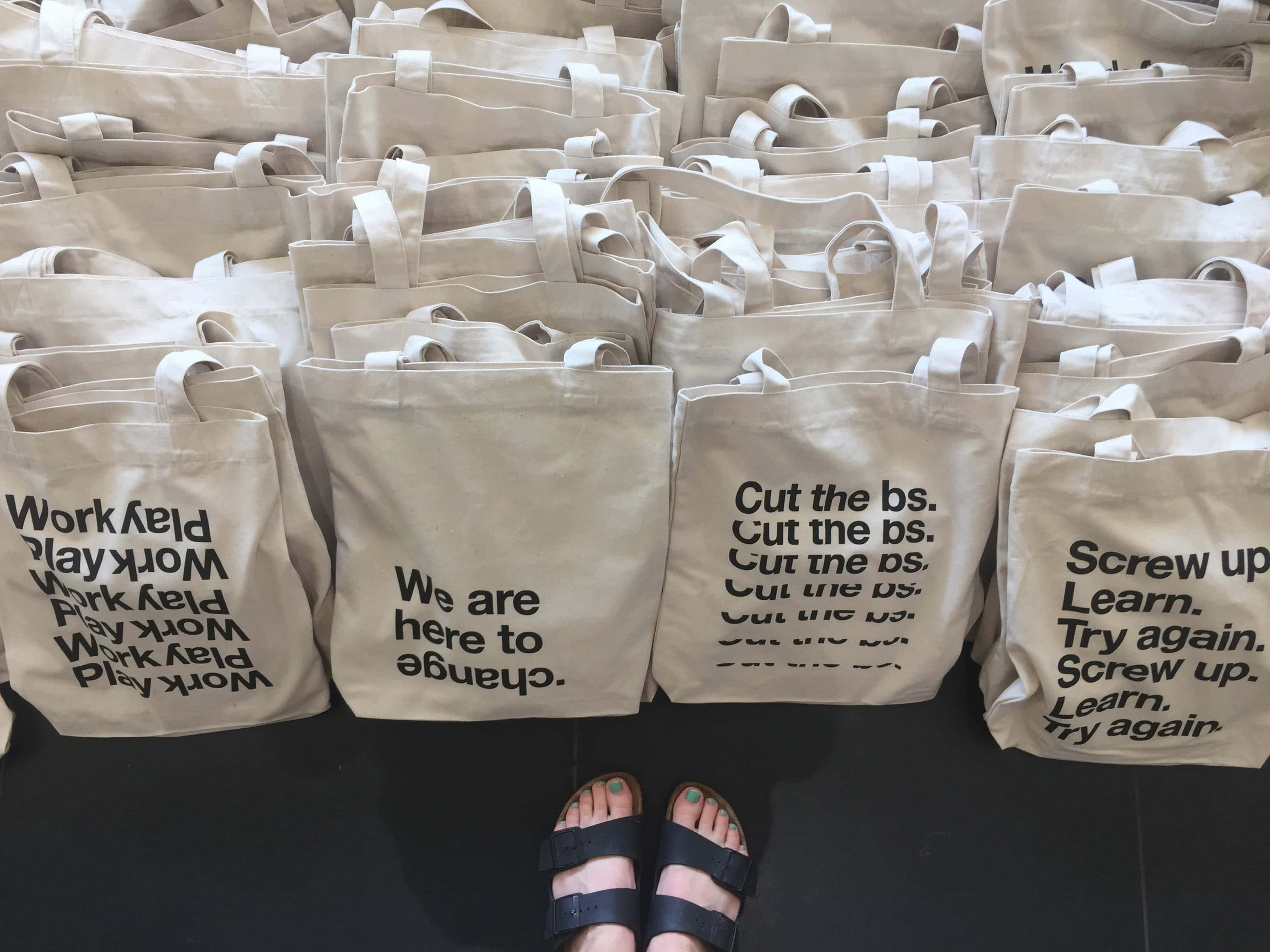 Tote bags displaying four different variations on “We are here”